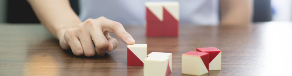 Une main déplace des cubes en bois partiellement peints en rouge selon des motifs triangulaires.